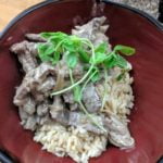Beef stroganoff with mushrooms and sauce served over rice in a red bowl, topped with green garnish