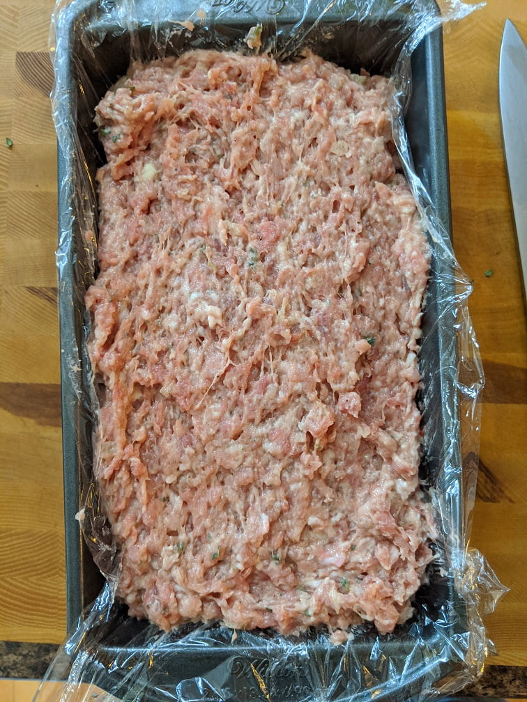 Loaf pan covered with foil over plastic wrap