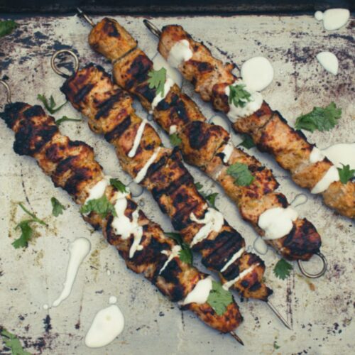 Four grilled tandoori chicken skewers with yogurt and cilantro