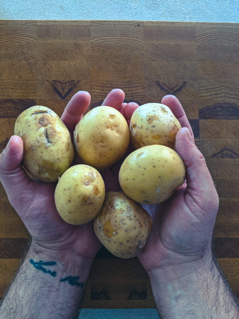 Whole yellow potatoes on a cutting board ready for peeling