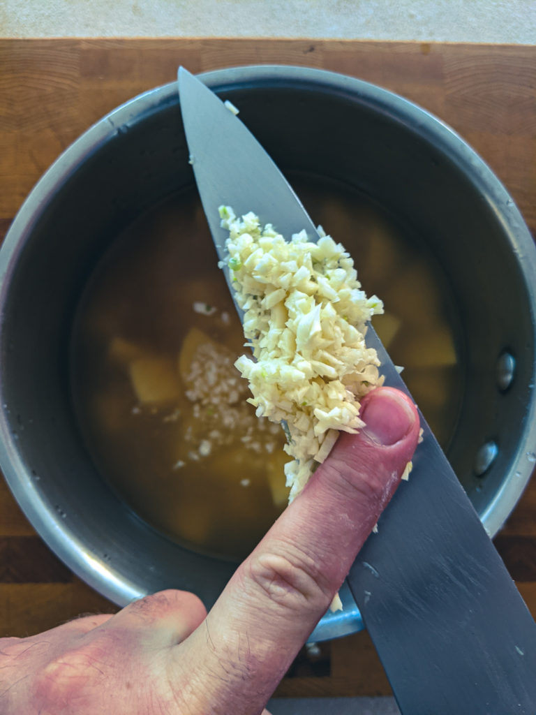 Adding butter to the pot with potatoes and stock