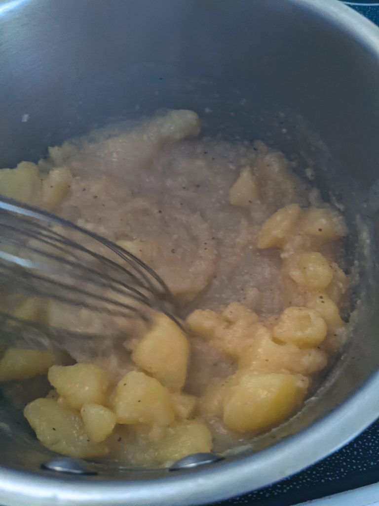 Whisking soft potatoes in the pot until smooth