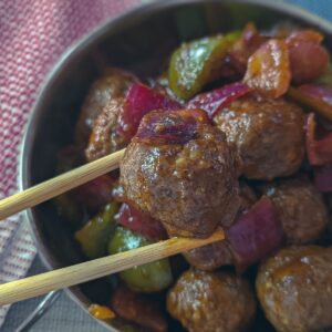 A bowl of sweet and sour meatballs with onions and peppers