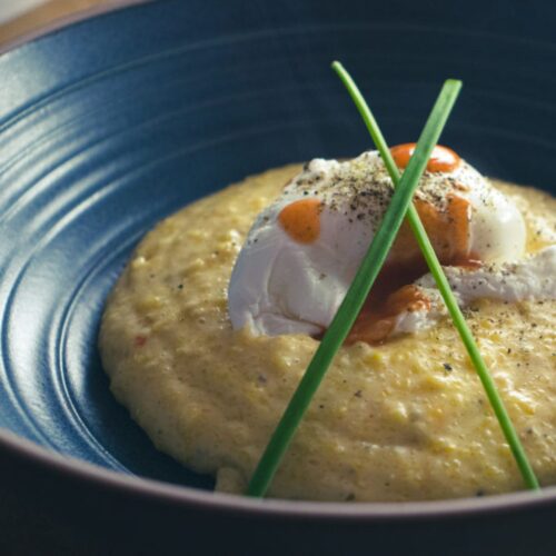 Bowl of cheesy polenta topped with a poach egg, hot sauce and chives
